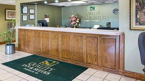 A hotel reception area with a wooden reception desk, a framed welcome sign, and a green doormat.