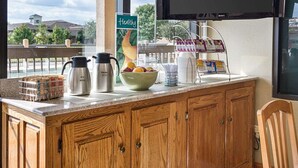 A kitchen counter with a coffee maker, a Skim milk bottle, a bowl of fruit, and a sign that says "Healthy."