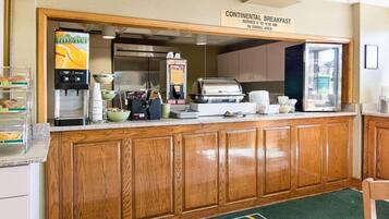 Un espace dédié au petit-déjeuner continental, équipé d’une machine à café, de boîtes de céréales et d’un panneau indiquant les heures de service.