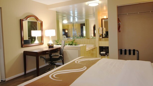 A hotel room with a bed, a desk, a chair, a mirror, and a bathroom visible through an open door.