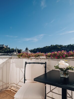 Une terrasse avec une table et une chaise, un vase rempli de fleurs, et une vue sur un château et une église en arrière-plan.