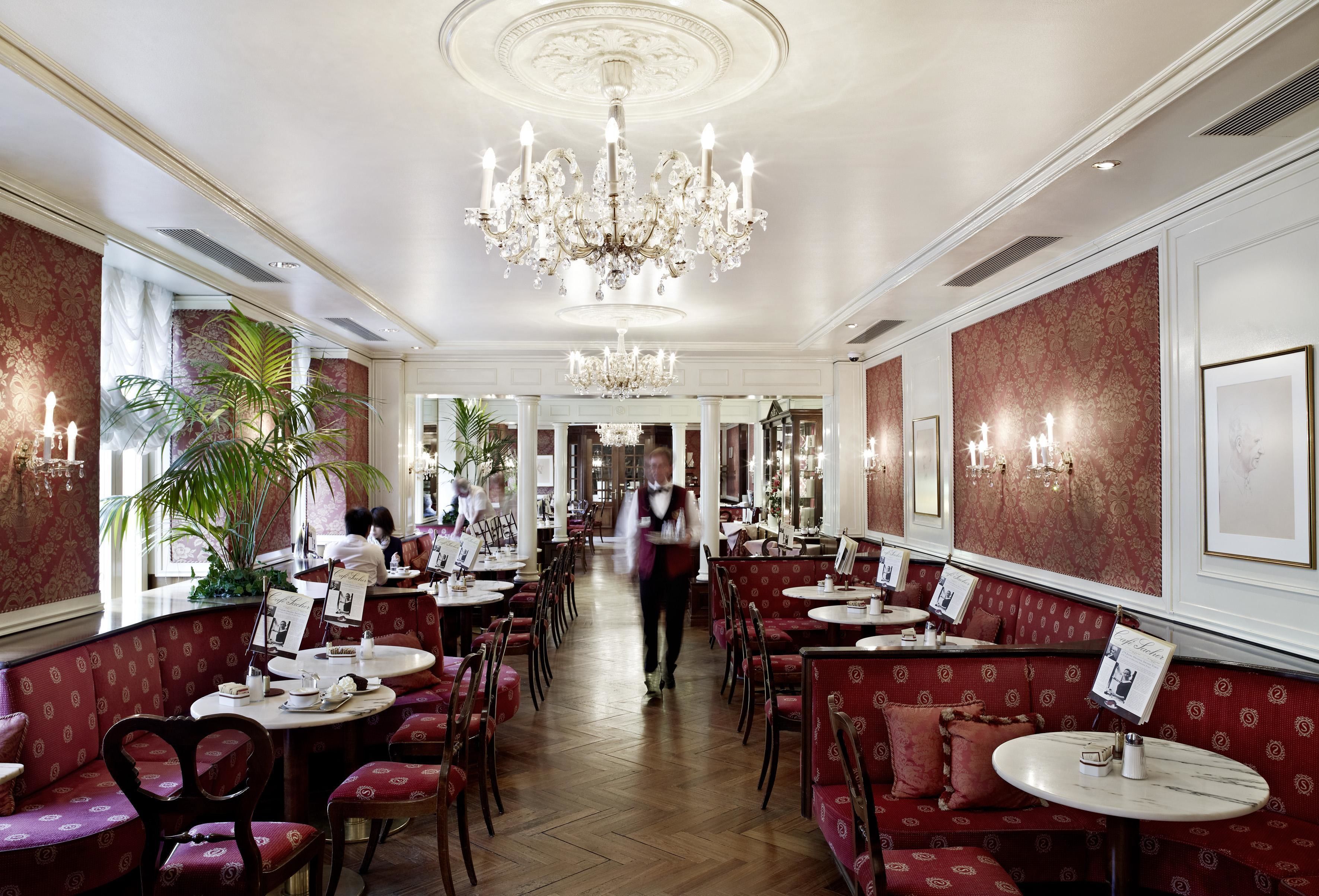 A spacious restaurant with high ceilings, ornate chandeliers, and red upholstered booths.