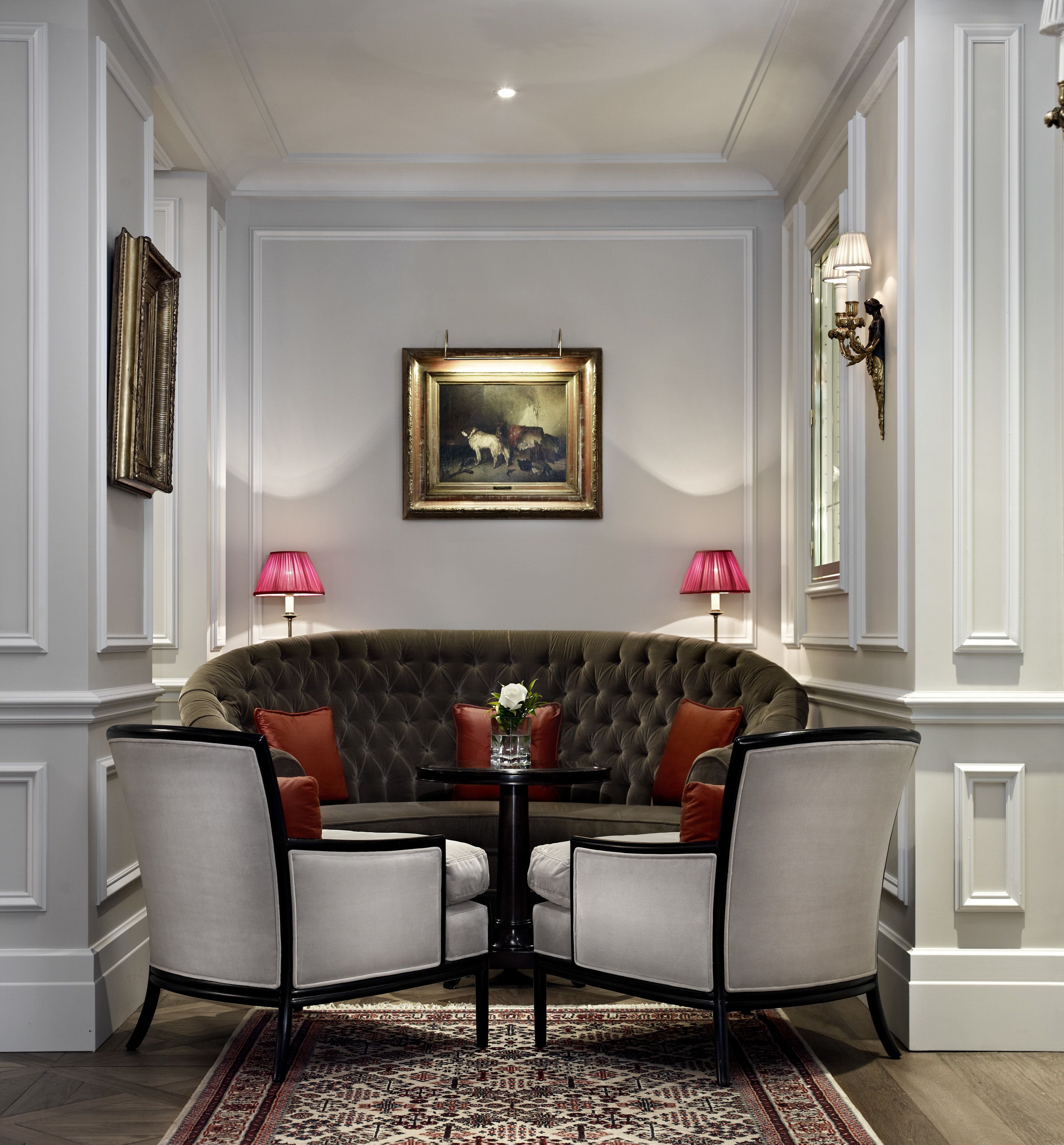 A formal room with a tufted sofa, two chairs, a small table, and a painting on the wall.