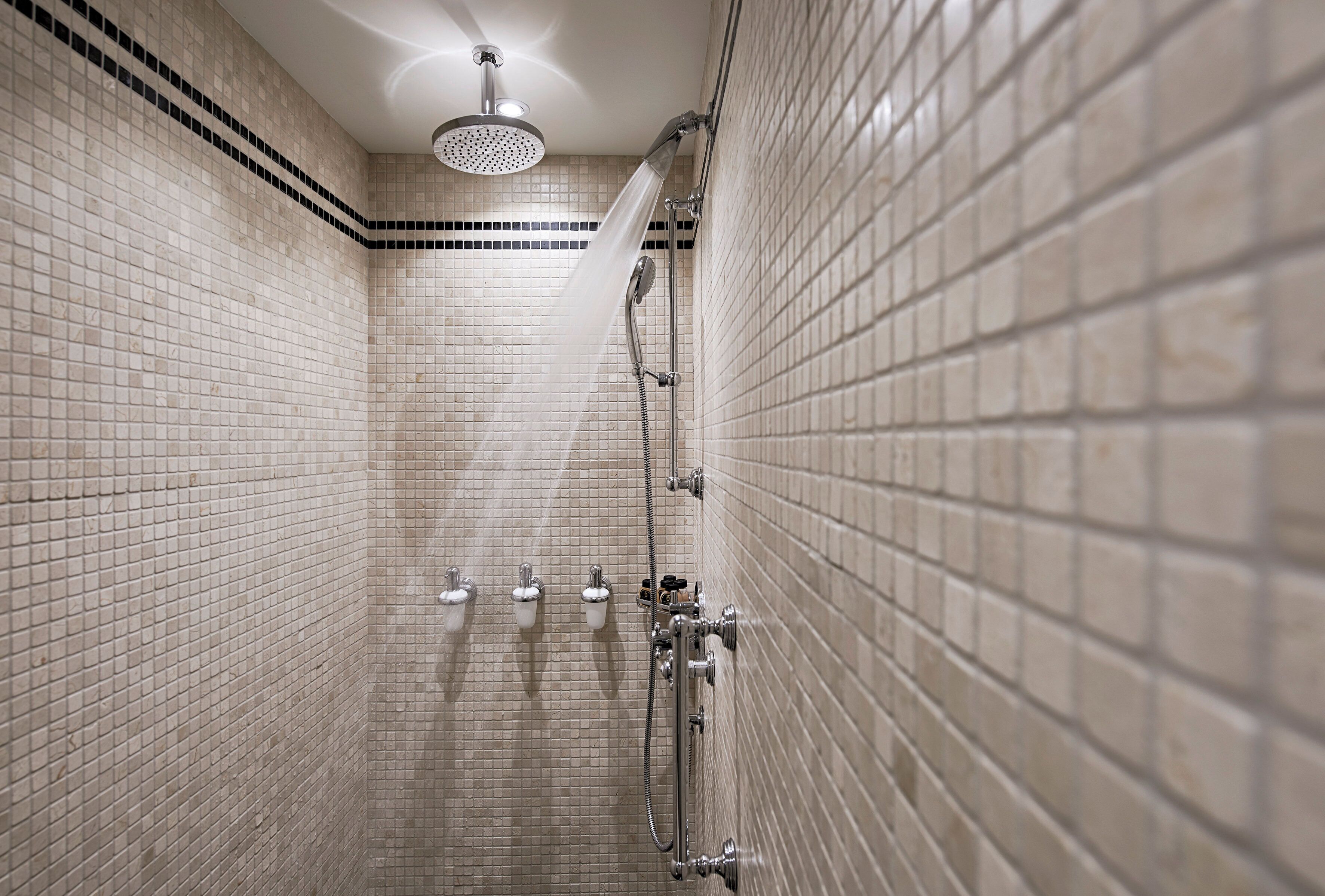 Eine geflieste Dusche mit Handbrause und am Wand montiertem Wasserhahn.