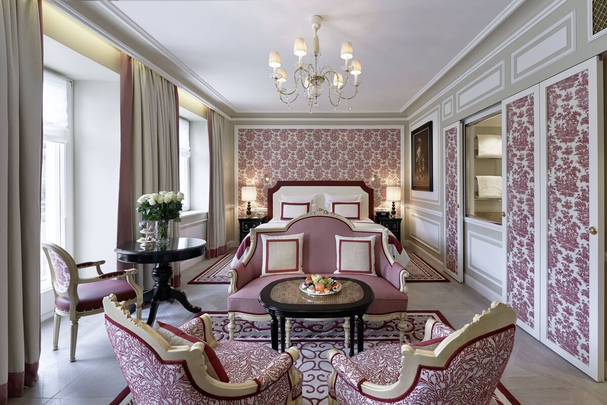A luxurious bedroom with a large bed, ornate chandelier, and floral wallpaper.