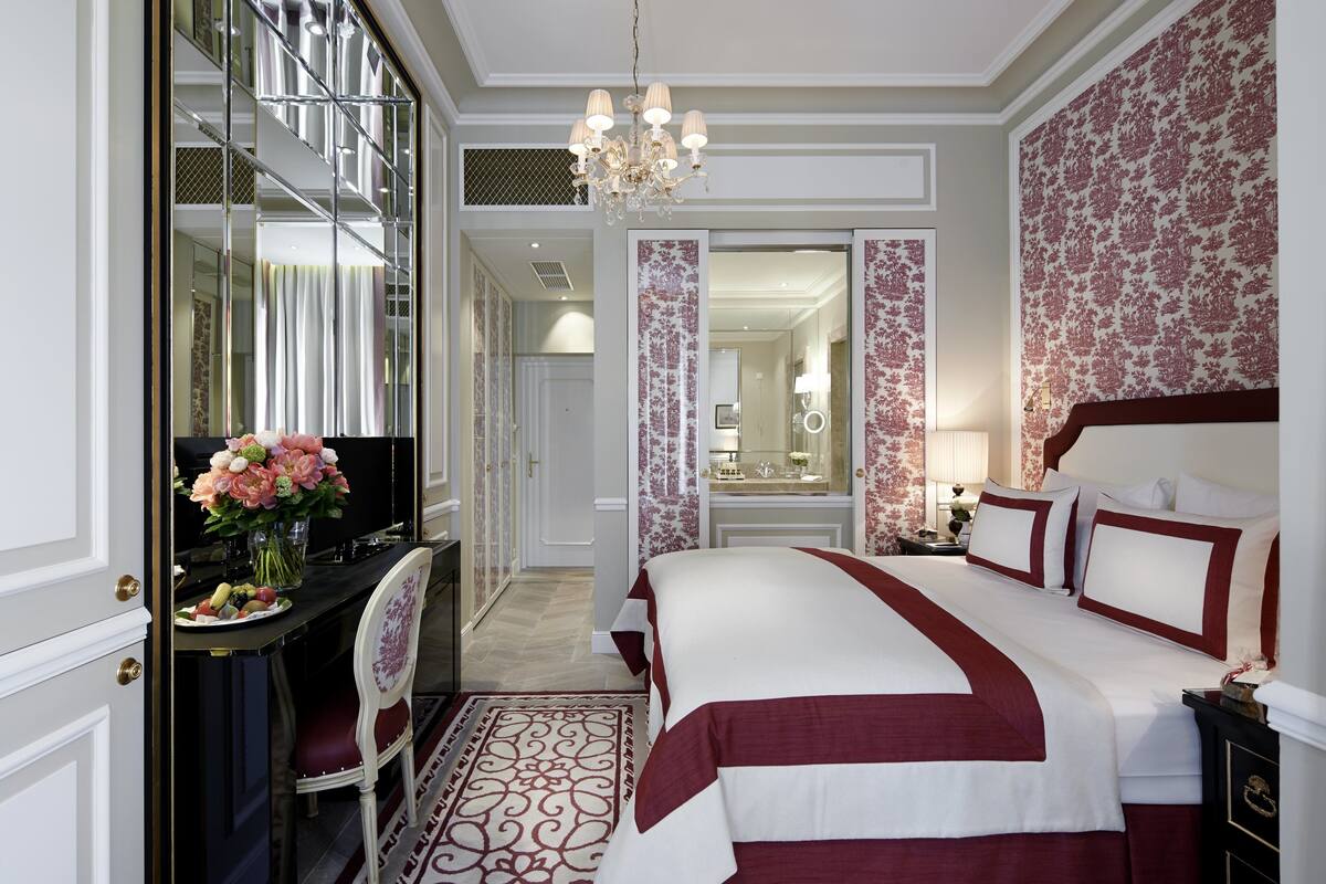 A hotel room with a large bed, a desk with a computer, a mirror, and a chandelier.