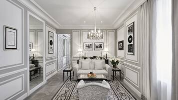 Uma sala de estar ampla com um sofá grande, uma mesa de centro e um candelabro. Há quadros nas paredes e um tapete estampado no chão.