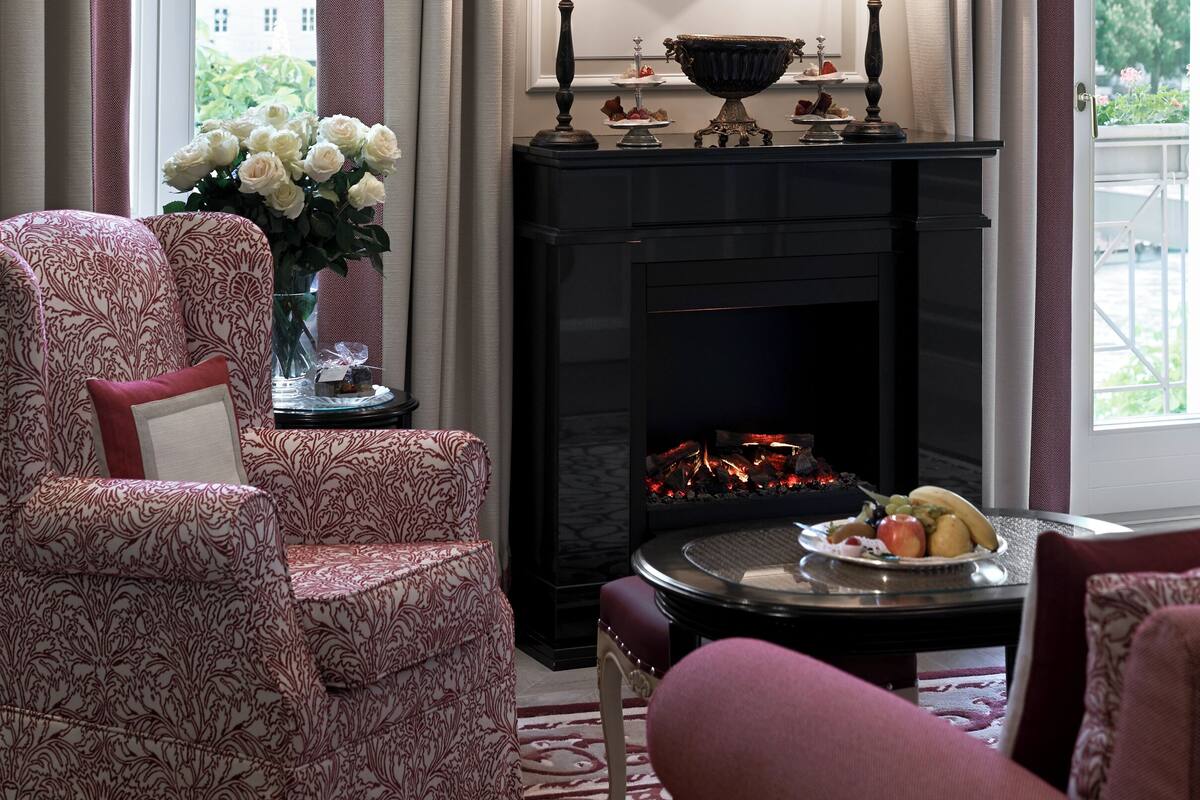 A living room with a fireplace, a chandelier, and a view of the city through large windows.