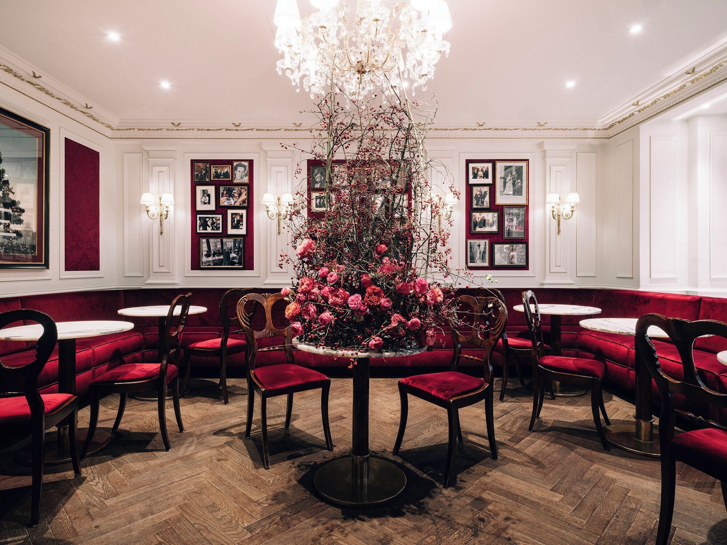 A formal dining room with red velvet booths, wooden chairs, and a central floral arrangement.