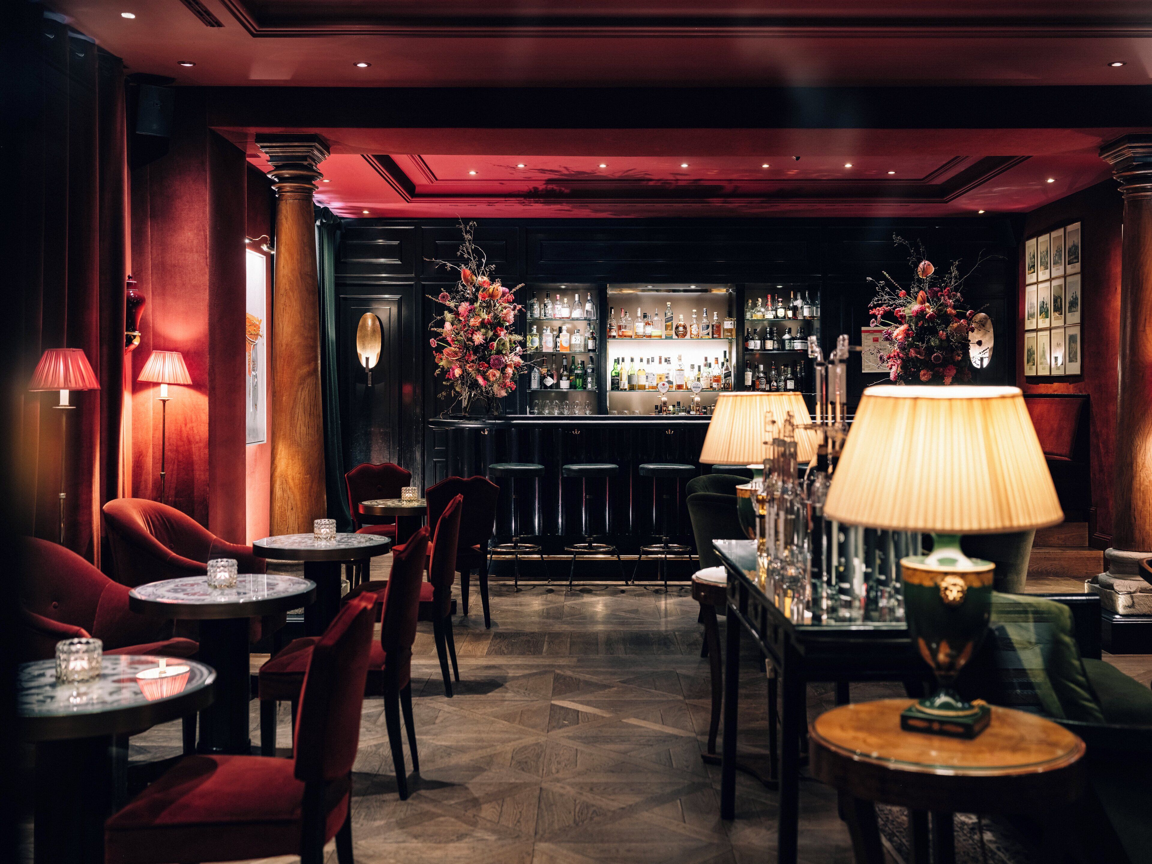 Eine Bar mit mehreren Tischen und Stühlen, einer Theke mit Flaschen und einer dekorativen Vase mit Blumen.