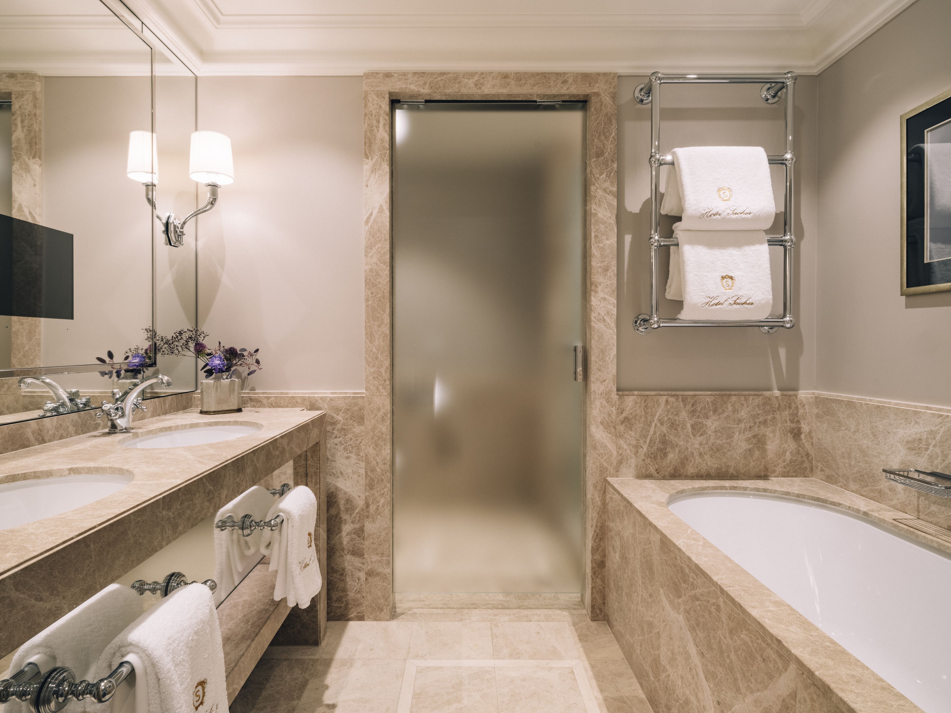 A modern bathroom with two sinks, a bathtub, a shower, and a glass door leading to a hallway.