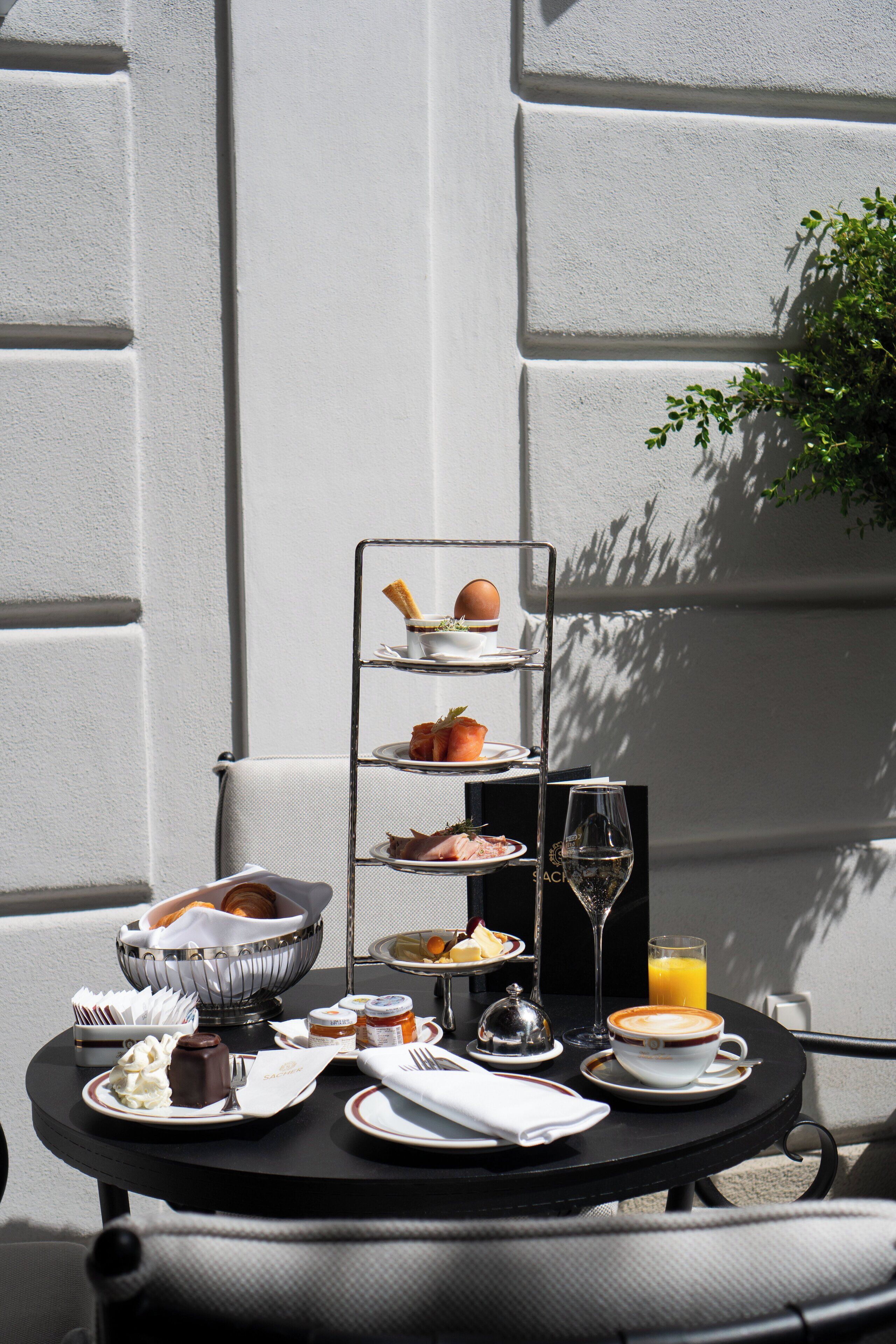 Een gedekte tafel met een etagère voor desserts, een schaal gebakjes, een glas sinaasappelsap en een kop koffie.