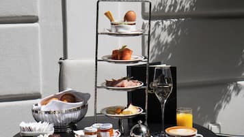 Een gedekte tafel met een etagère voor desserts, een schaal gebakjes, een glas sinaasappelsap en een kop koffie.