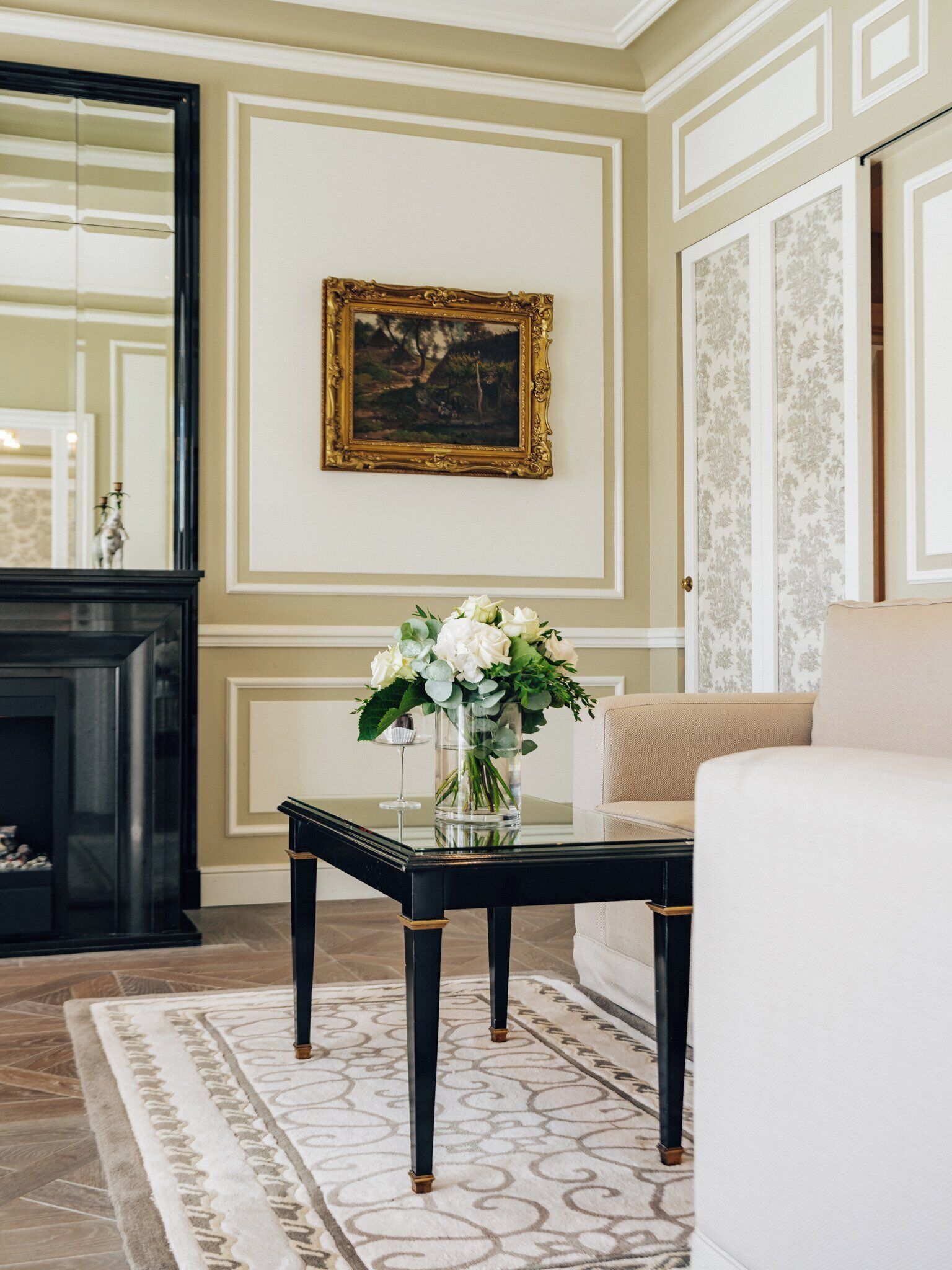 A living room with a fireplace, a sofa, a coffee table with a vase of flowers, and a framed painting on the wall.