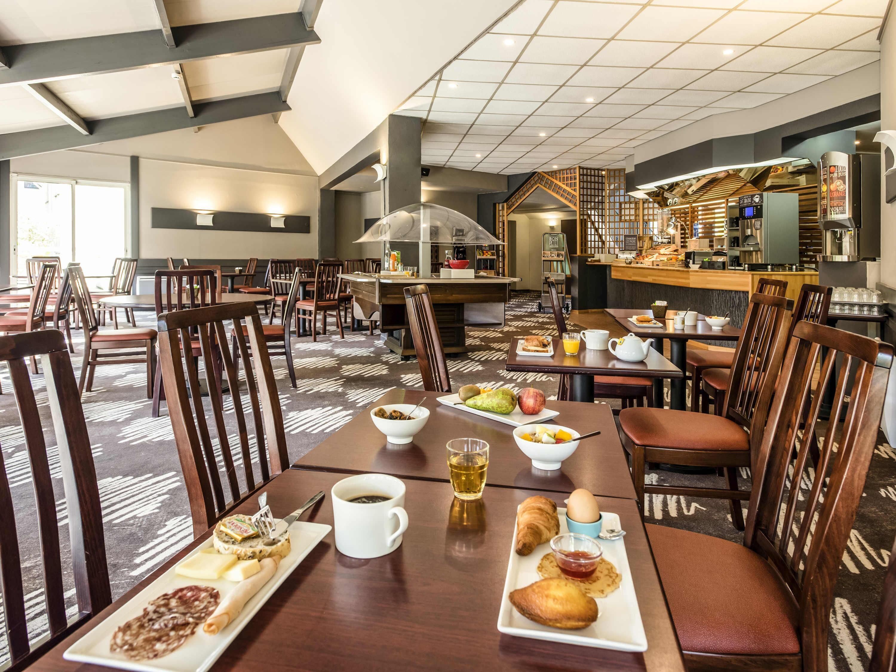 Un comedor de hotel con varias mesas, sillas y una cocina al fondo.