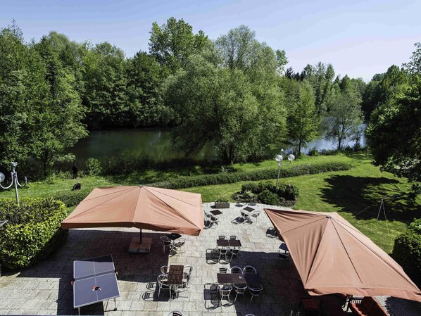 Ett utomhusområde med sittplatser, bord och stolar, ett bordtennisbord och parasoller.