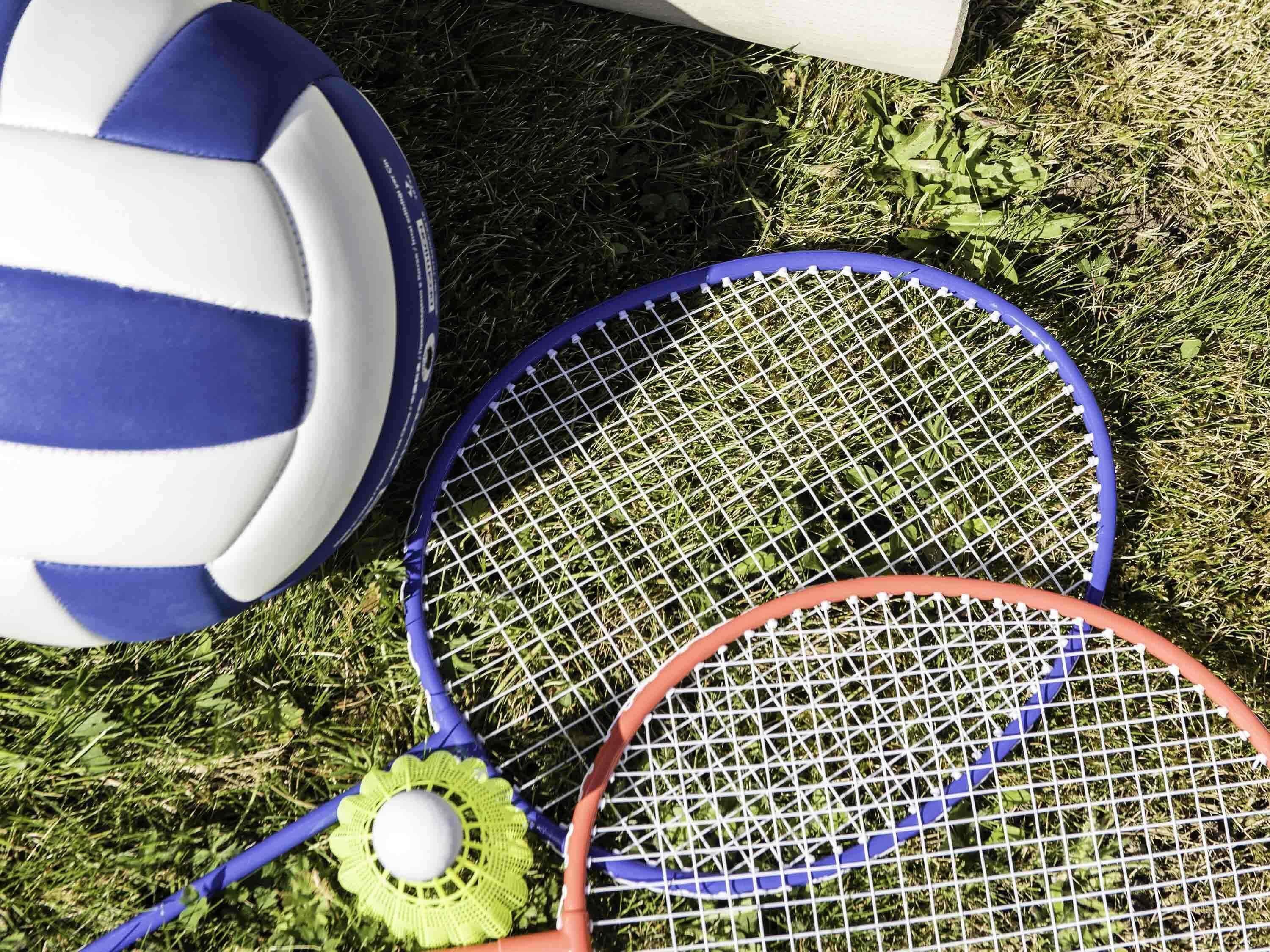 Una pelota de voleibol, dos raquetas de tenis y un volante verde sobre césped.