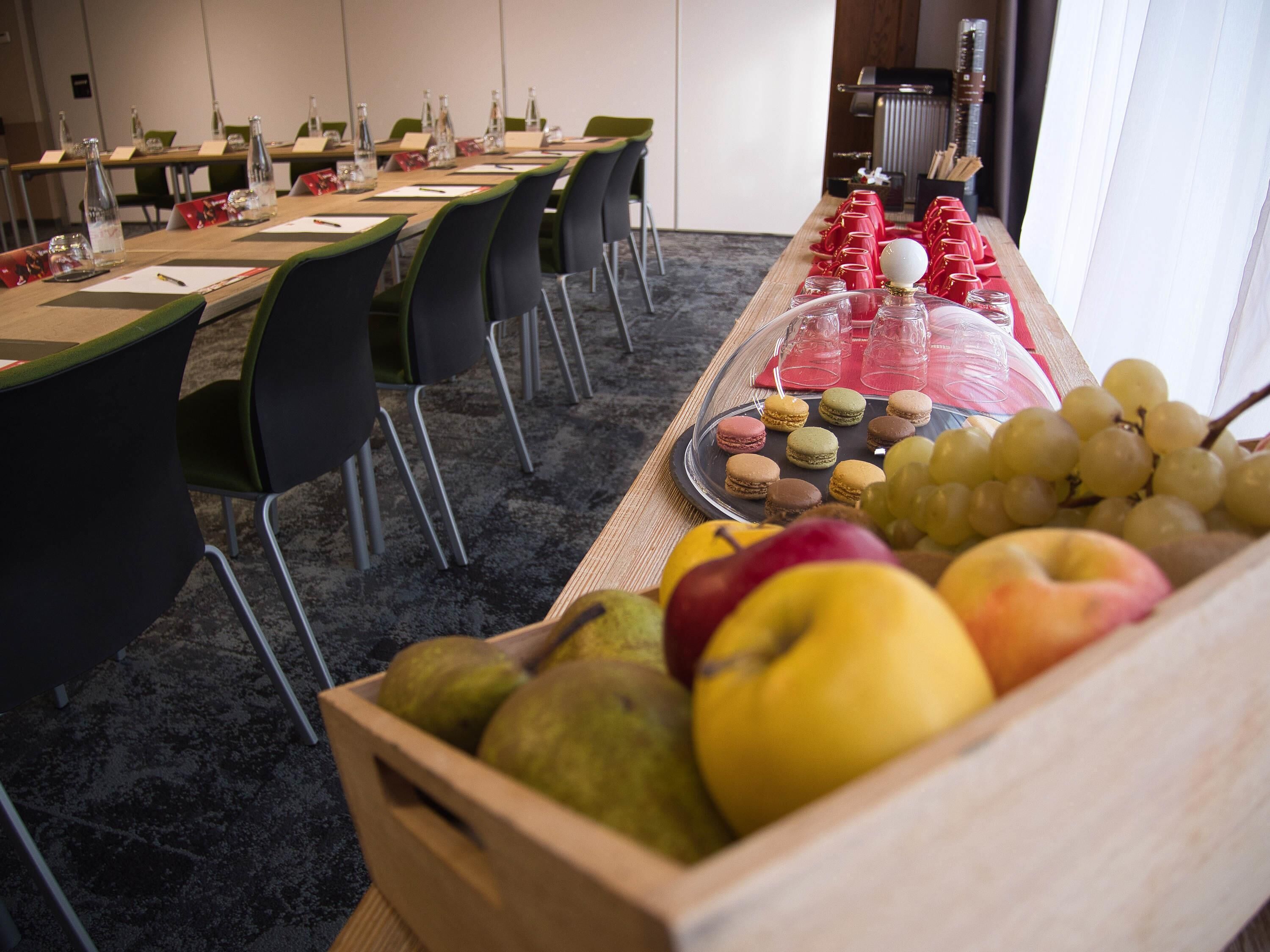 Un salón de conferencias con una larga mesa, sillas y una bandeja de fruta.