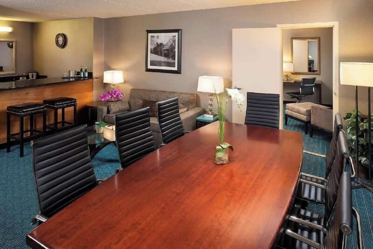 A hotel conference room with a large wooden table, several chairs, a sofa, a small bar area, and a mirror.
