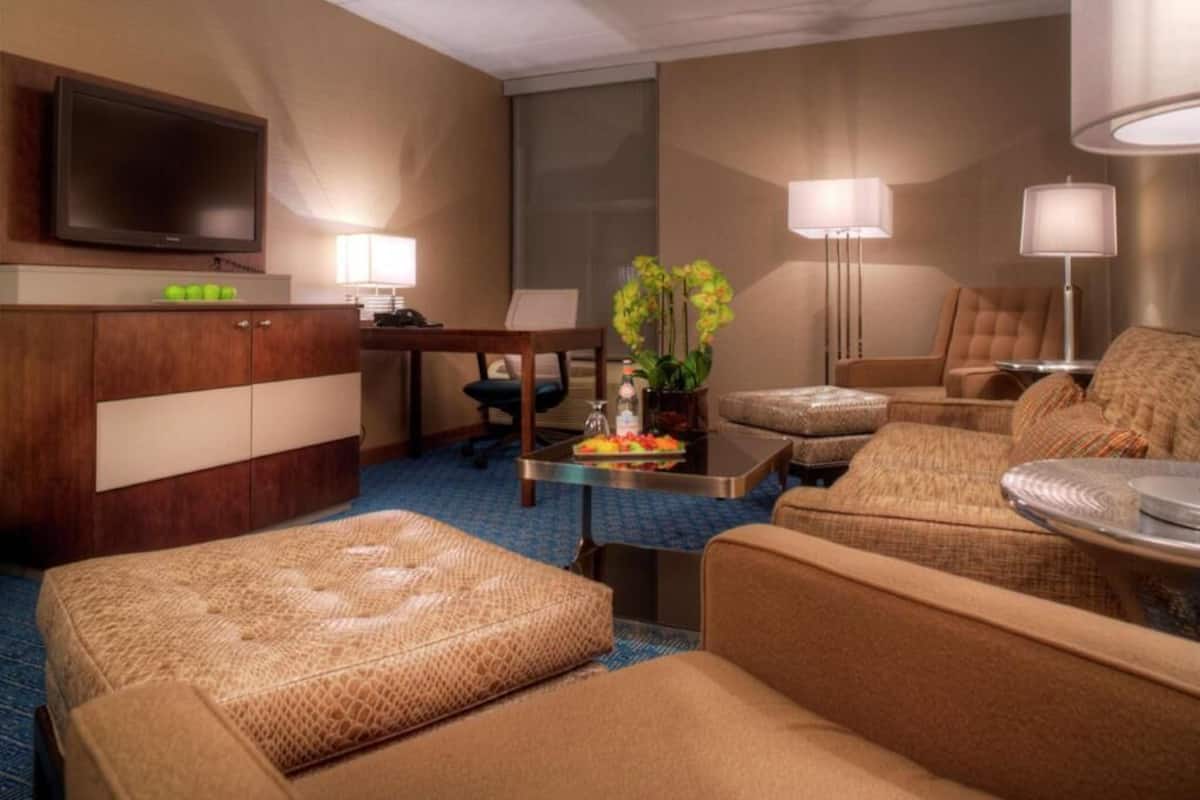 A hotel room with a flat-screen TV, a desk, a sofa, a chair, and a lamp.