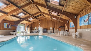 Ein großes Hallenbad mit Holzbalken, weißen Liegestühlen und einem Empfangsbereich mit einer Uhr.