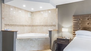 Ein Hotelzimmer mit einer großen Badewanne, einem Bett, einem Nachttisch mit Lampe und einem Spiegel an der Wand.