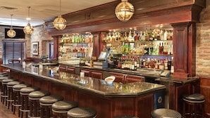 Eine Bar mit einer langen Theke, Hockstühlen und einer Auswahl an Flaschen.