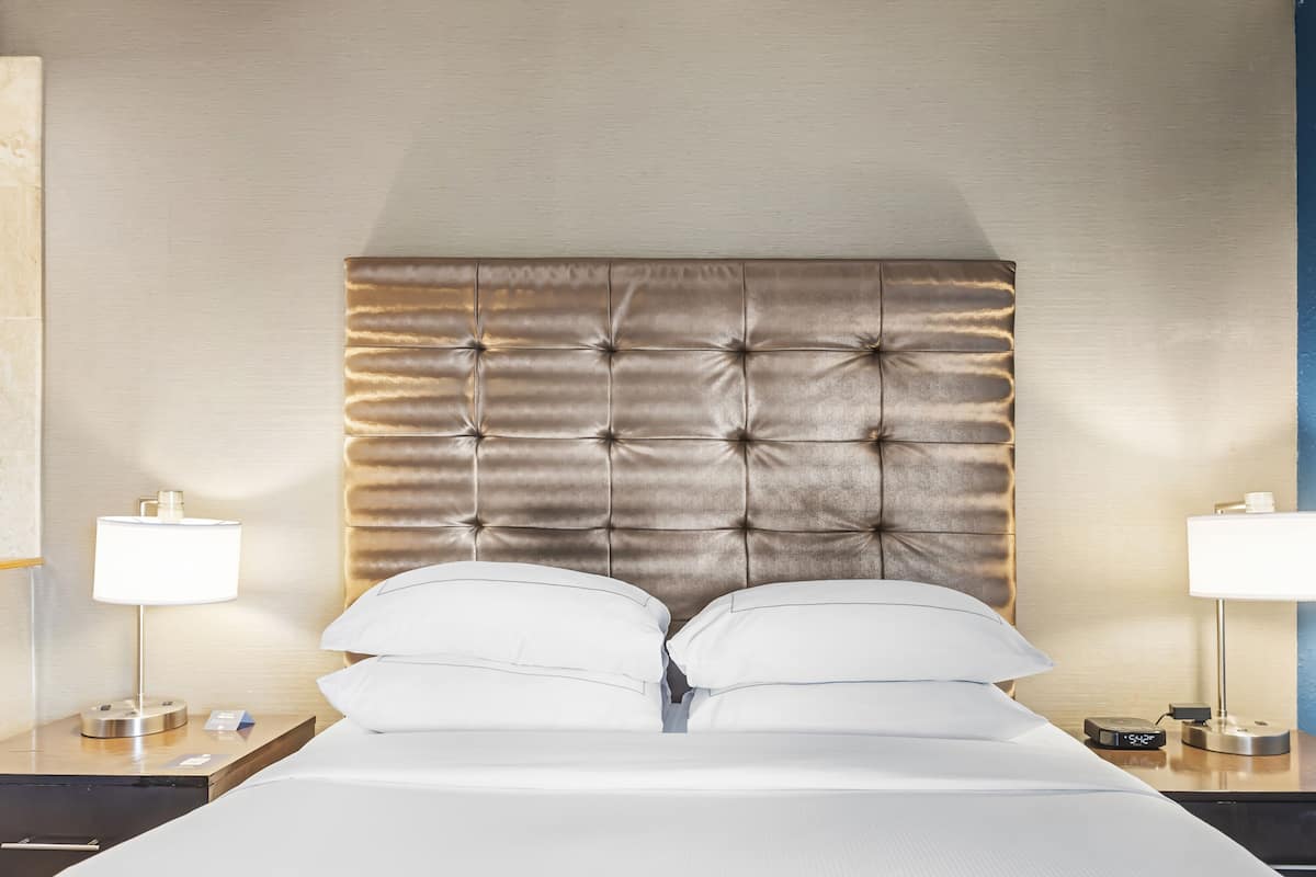 A neatly made bed with a tufted headboard, two bedside tables with lamps, and a wall with a textured finish.