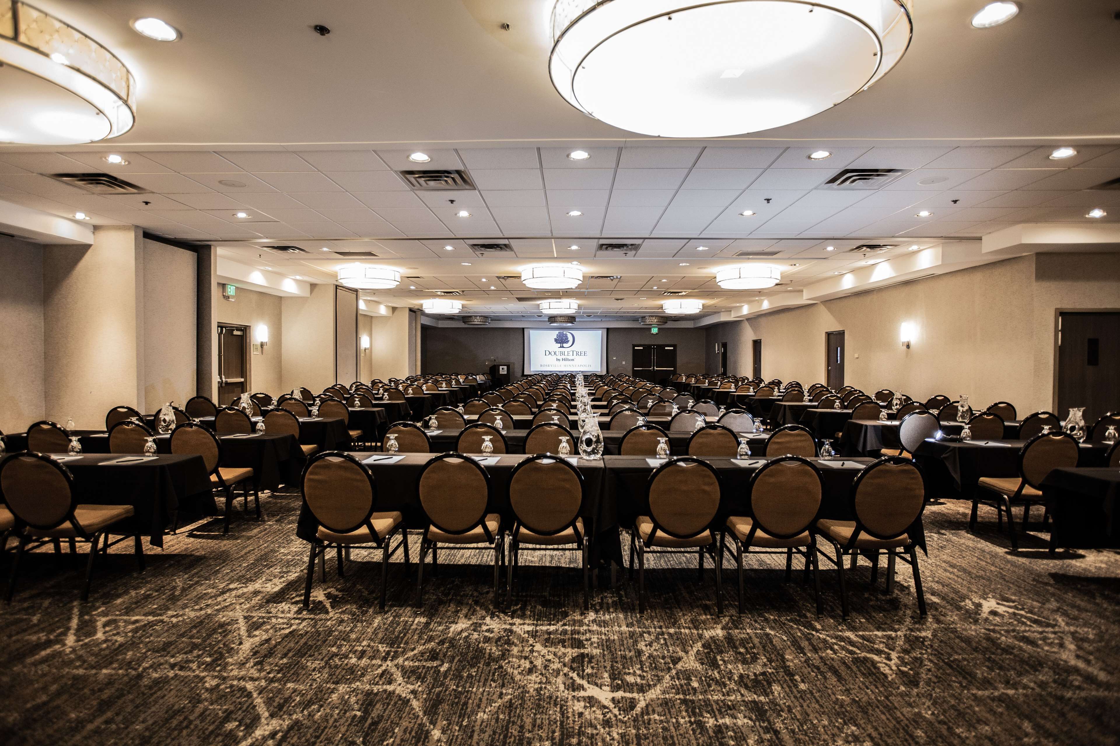 A large conference room with rows of tables and chairs, equipped with nameplates and water glasses.
