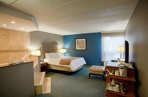 A hotel room with a bed, bedside tables, a desk, a chair, a window with curtains, and a wall-mounted artwork.