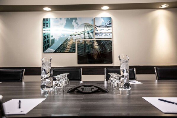 A conference room with a wooden table, glassware, and a phone. There are chairs around the table, and a wall with a framed picture.