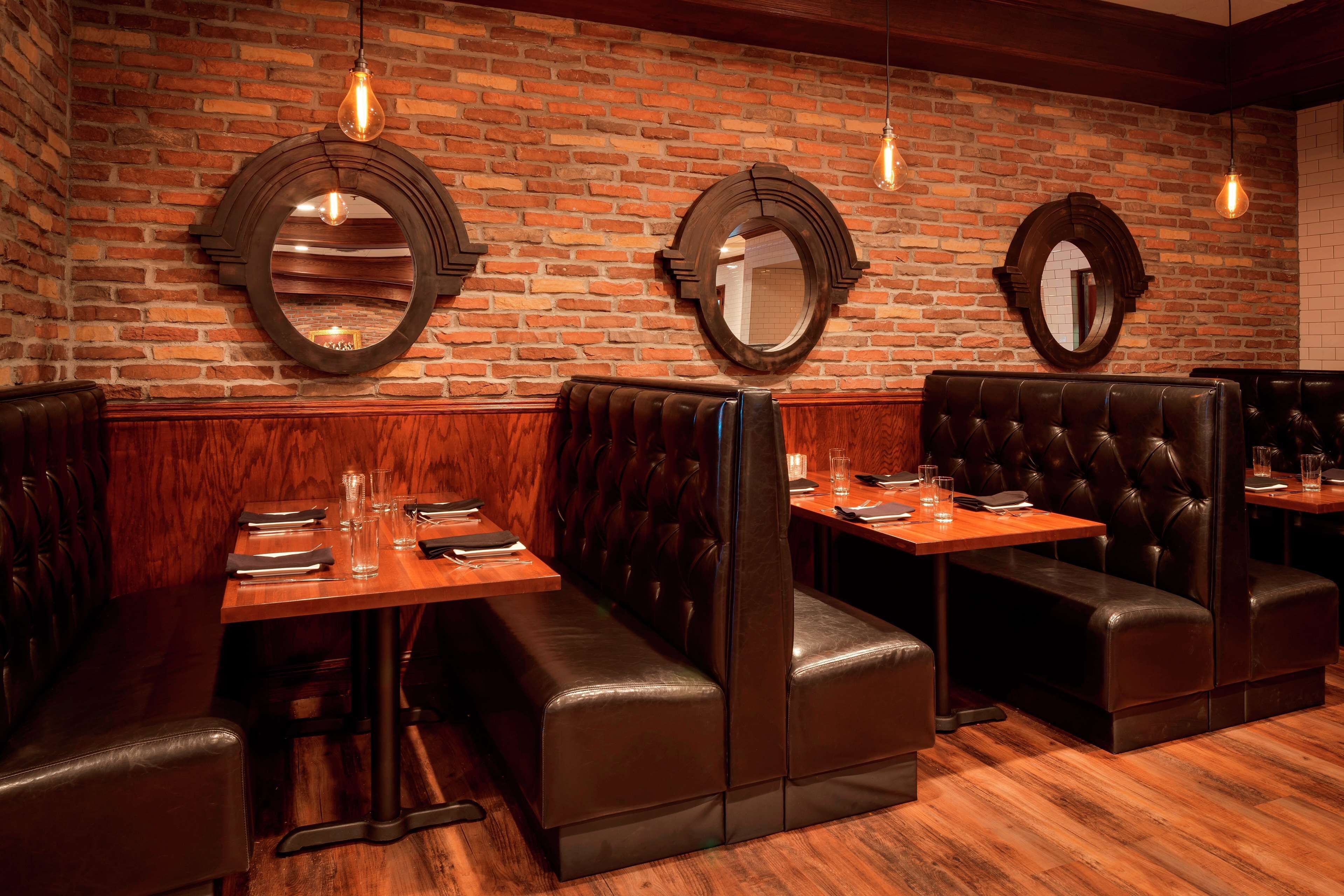 A restaurant interior with brick walls, wooden flooring, and leather booths.