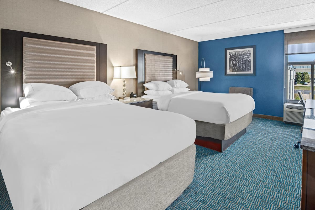 A hotel room with two beds, a desk, a chair, a window with a view, and a blue patterned carpet.