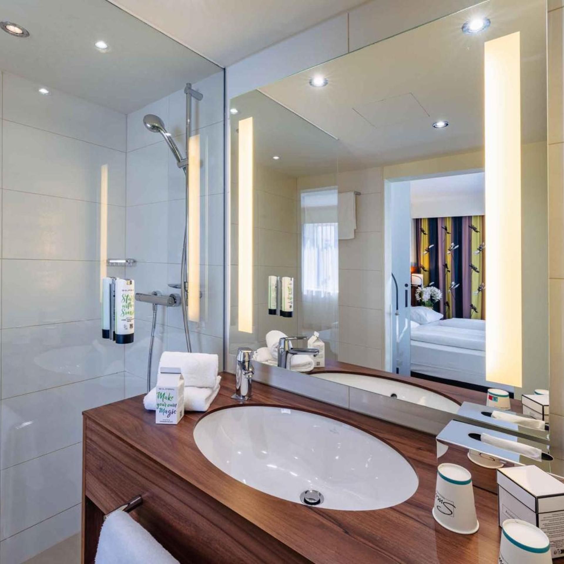 Un baño moderno con un espejo grande, un tocador de madera, un lavabo y una ducha.