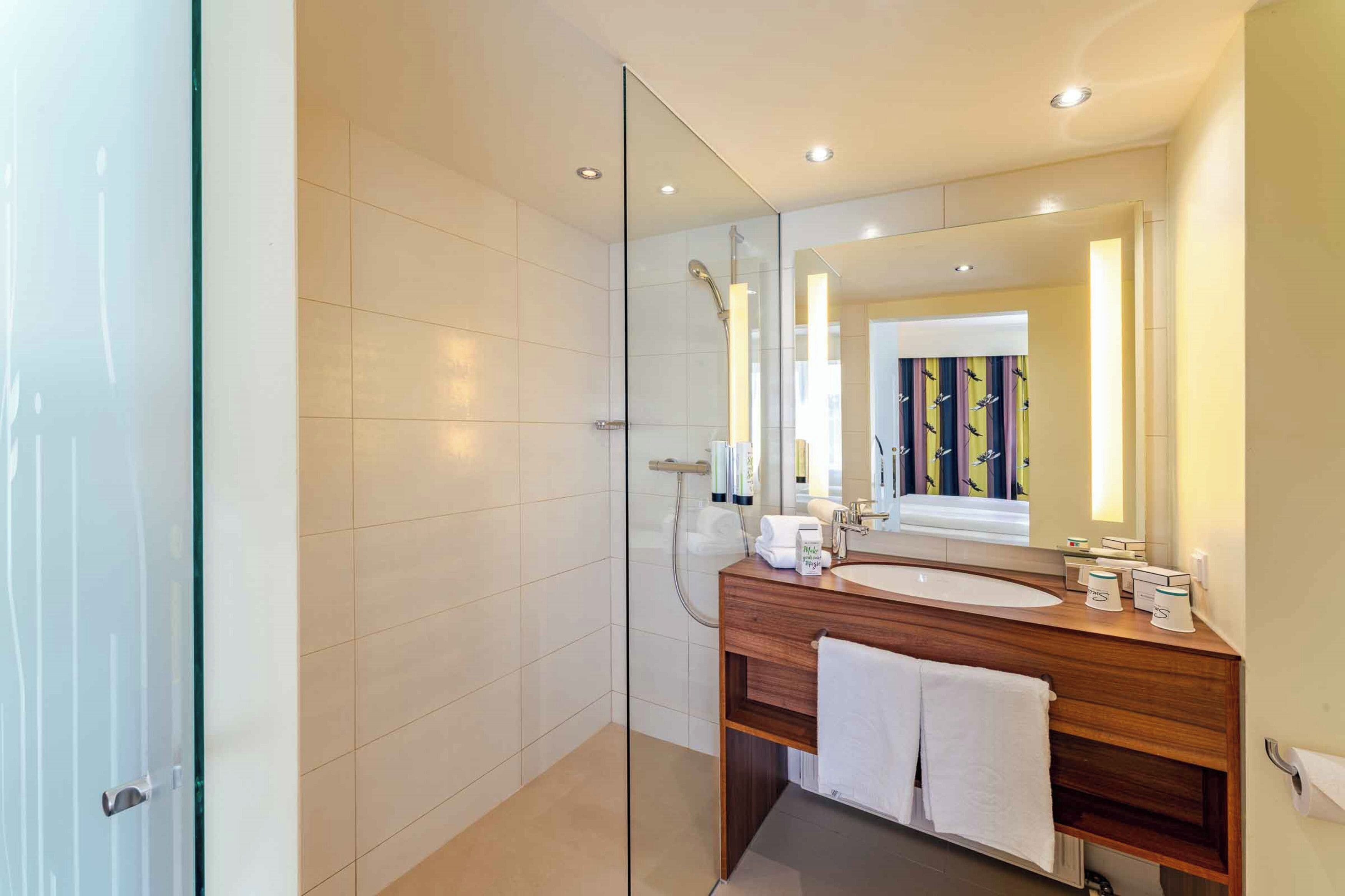 A modern bathroom with a glass-enclosed shower, a wooden vanity with a sink, and a large mirror.