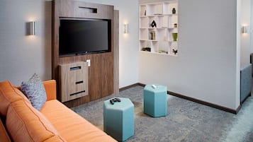 Una sala de estar moderna con un televisor de pantalla plana montado en un mueble de madera, un sofá, dos otomanas y un estante de pared con objetos decorativos.
