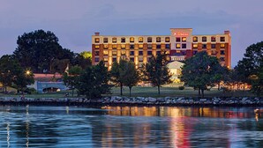A hotel with a large building, a body of water in front, and trees around. - Hilton Garden Inn Providence (Providence)
