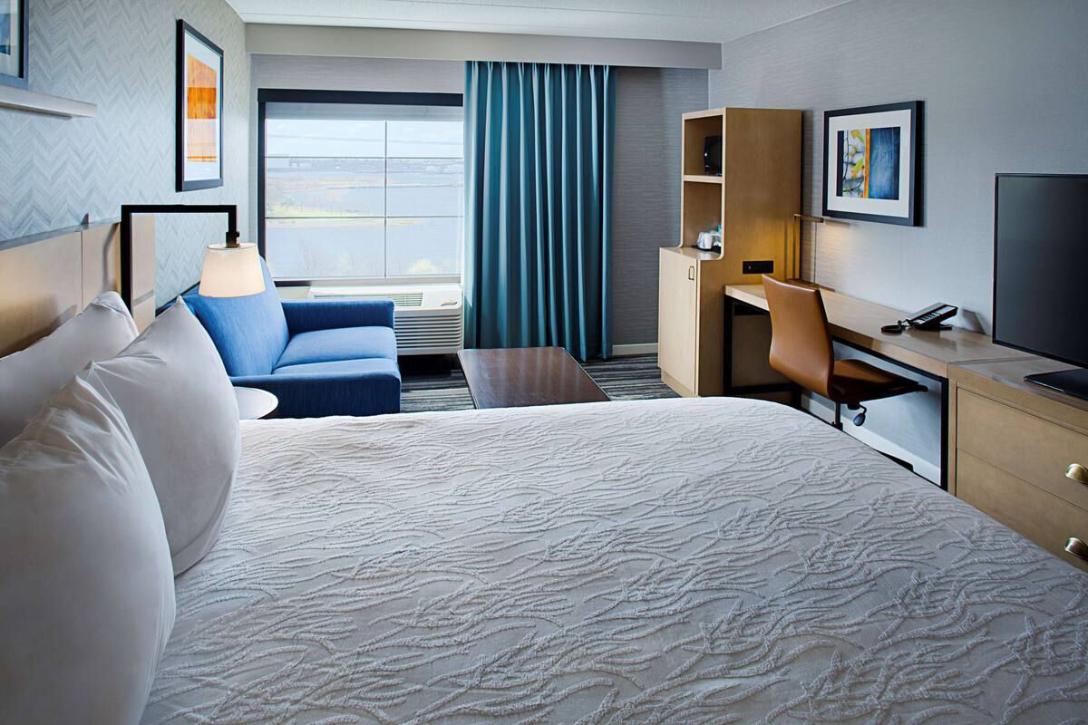 A hotel room with a large bed, a desk, a chair, a TV, and a window with curtains.