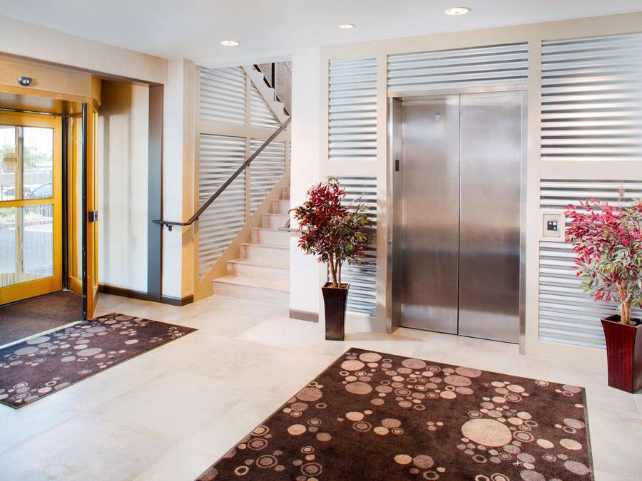 Een moderne hotel lobby met een trap, een lift en twee potplanten.