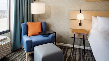 A hotel room with a sofa, ottoman, two bedside tables with lamps, a bed, and a window with curtains.