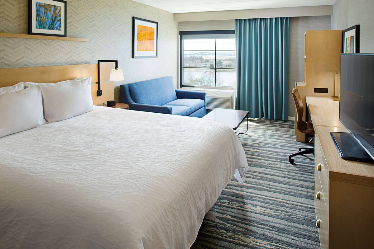 A hotel room with a large bed, a blue sofa, a desk with a computer, and a TV.