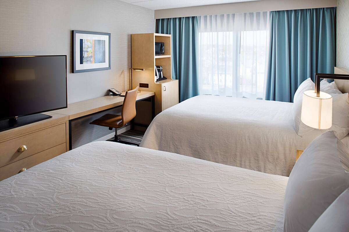 A hotel room with two beds, a desk with a chair, a television, and a window with curtains.
