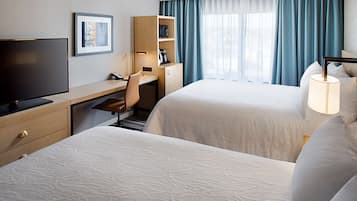 A hotel room with two beds, a desk with a chair, a television, and a window with curtains.
