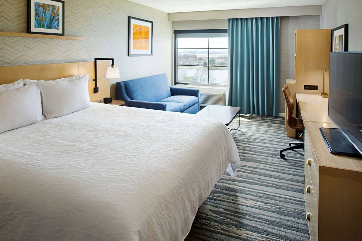 A hotel room with a large bed, a blue sofa, a desk with a laptop, and a TV.