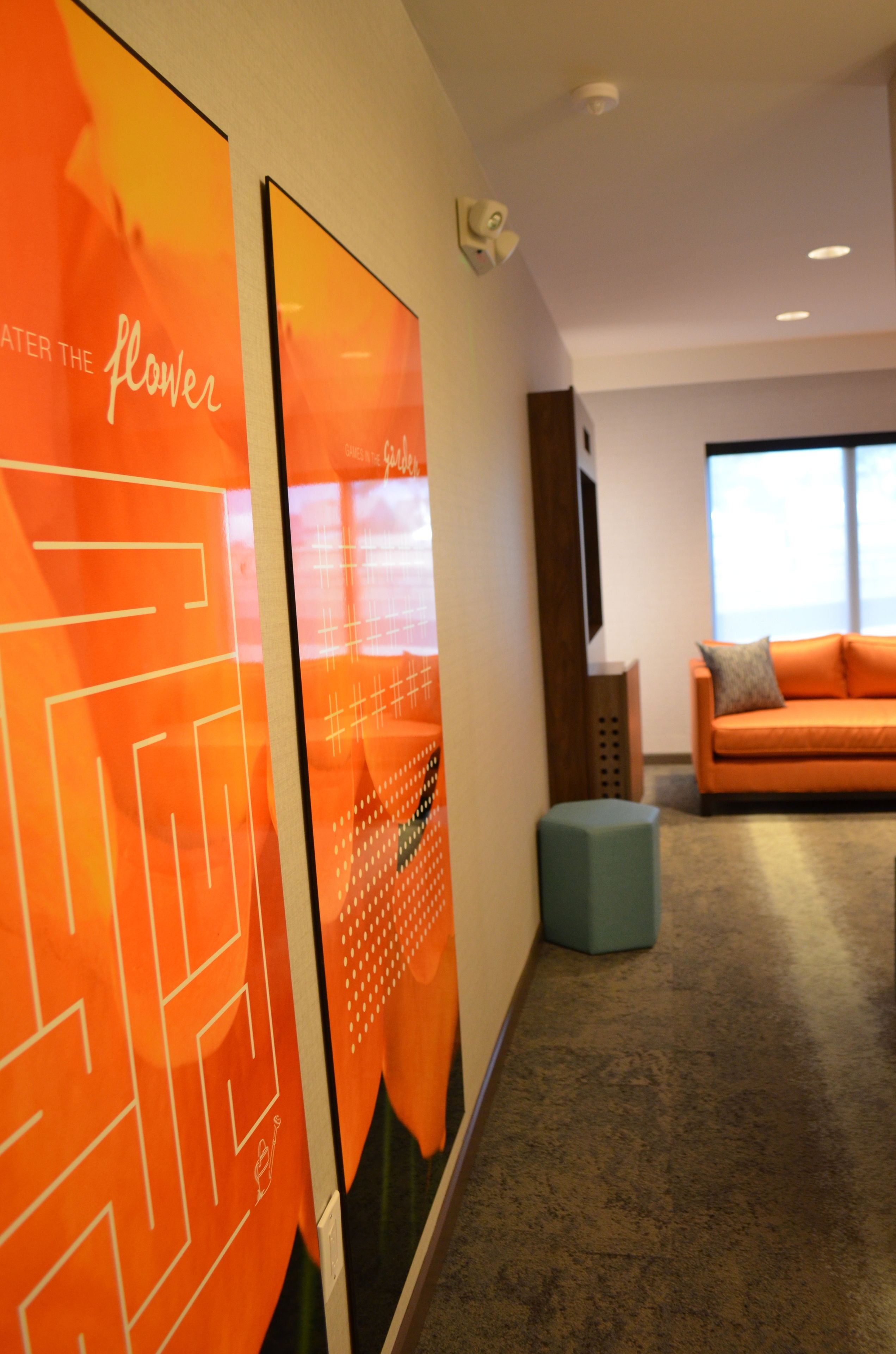 A modern interior with a large orange wall art piece, a grey ottoman, and an orange sofa in a well-lit room with a large window.