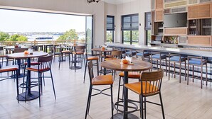 A spacious outdoor dining area with multiple tables and chairs, a bar with a large screen, and a view of a body of water. - Hilton Garden Inn Providence (Providence)