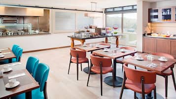 Un comedor moderno con varias mesas y sillas, una zona de cocina con bufé y amplias ventanas con vistas.