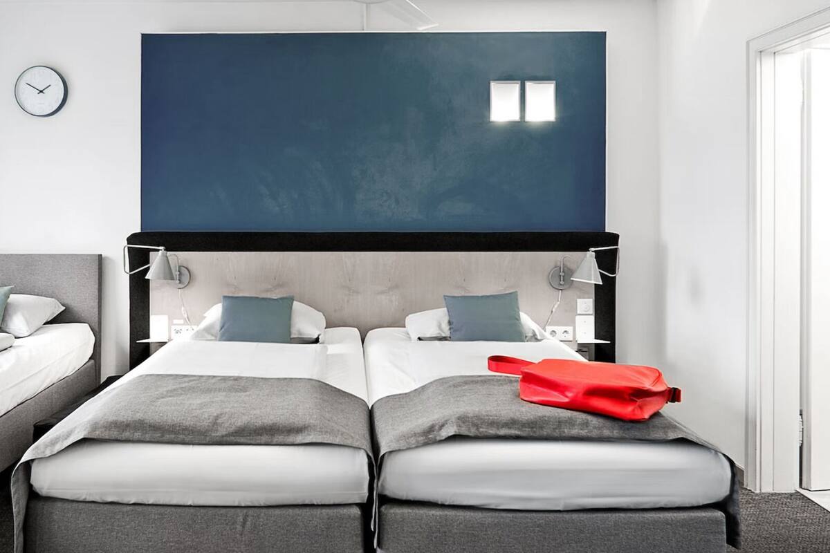 A modern hotel room with two beds, a large dark blue accent wall, and a clock on the wall.