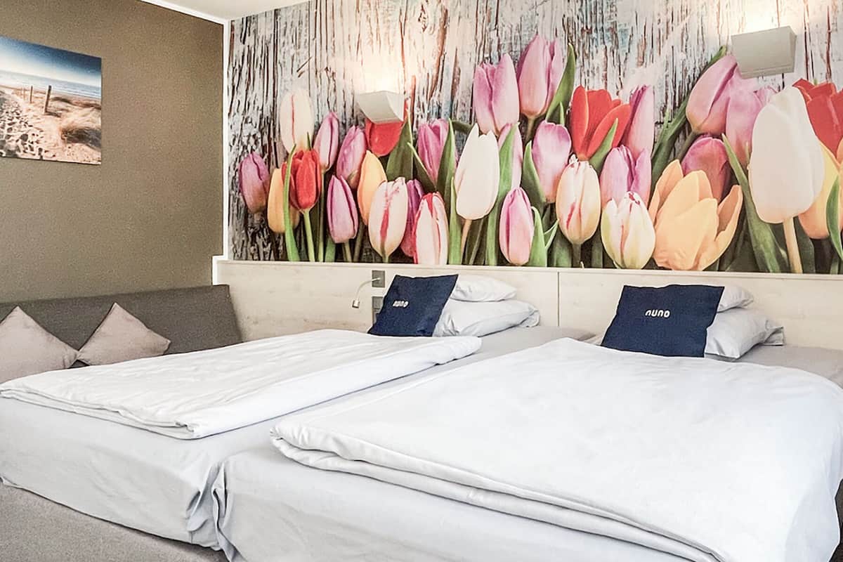 A hotel room with two beds, a large floral mural on the wall, and a painting of a beach scene.