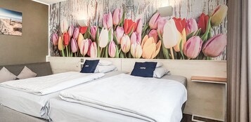 Una habitación de hotel con dos camas, un gran mural floral en la pared y una pintura de una playa.
